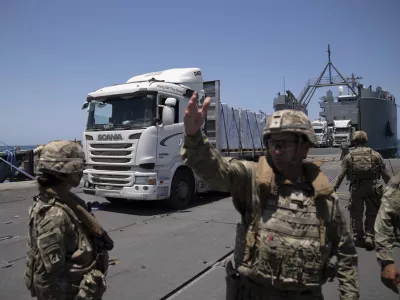 A U.S. Army soldier gestures as trucks loaded with humanitarian aid arrive at the U.S.-built floating pier Trident before reaching the beach on the coast of the Gaza Strip, Tuesday, June 25, 2024. (AP Photo/Leo Correa)