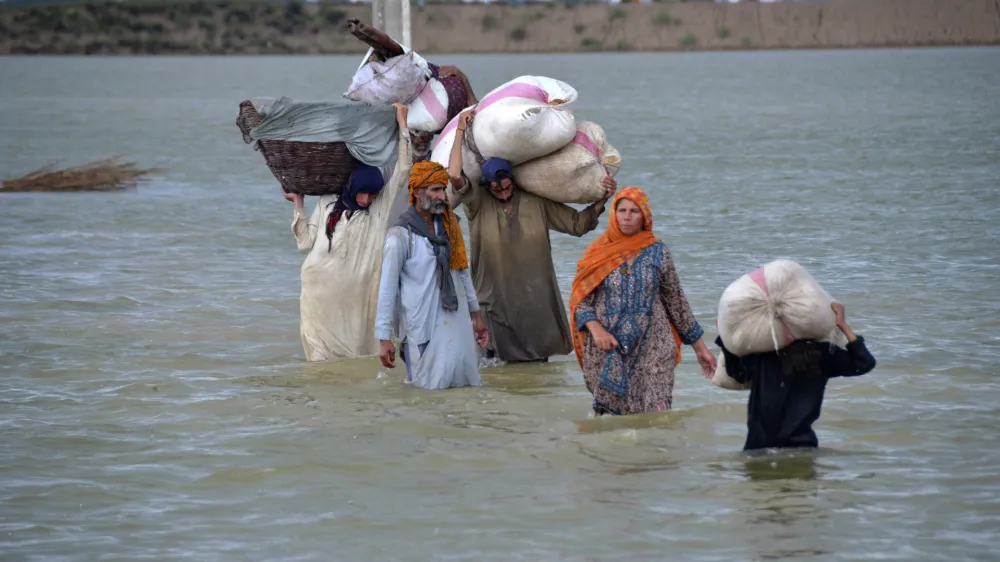 FILE - A displaced family wades through a flooded area after heavy rainfall, in Jaffarabad, a district of Pakistan's southwestern Baluchistan province, Aug. 24, 2022. A new study says human-caused climate change juiced the rainfall that triggered Pakistan's floods by up to 50%. But the authors of the Thursday, Sept. 15, study say other societal issues that make the country vulnerable and put people in harm's way are probably the biggest factor in the ongoing humanitarian disaster. (AP Photo/Zahid Hussain, File)