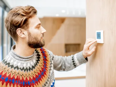 Man in sweater feeling cold adjusting room temperature with electronic thermostat at home