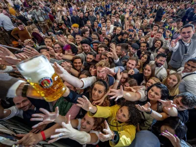 Young people reach out for free beer in one of the beer tents on the opening day of the 187th Oktoberfest beer festival in Munich, Germany, Saturday, Sept. 17, 2022. (AP Photo/Michael Probst)