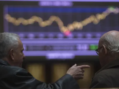 Traders talk in front of a screen showing an index at Madrid's Bourse February 14, 2012. European shares fell on Tuesday after rating agency Moody's put the United Kingdom's triple-A rating in jeopardy for the first time and warned it may cut France and Austria as well, while downgrading six euro zone nations including Spain and Italy. REUTERS/Sergio Perez (SPAIN - Tags: BUSINESS)