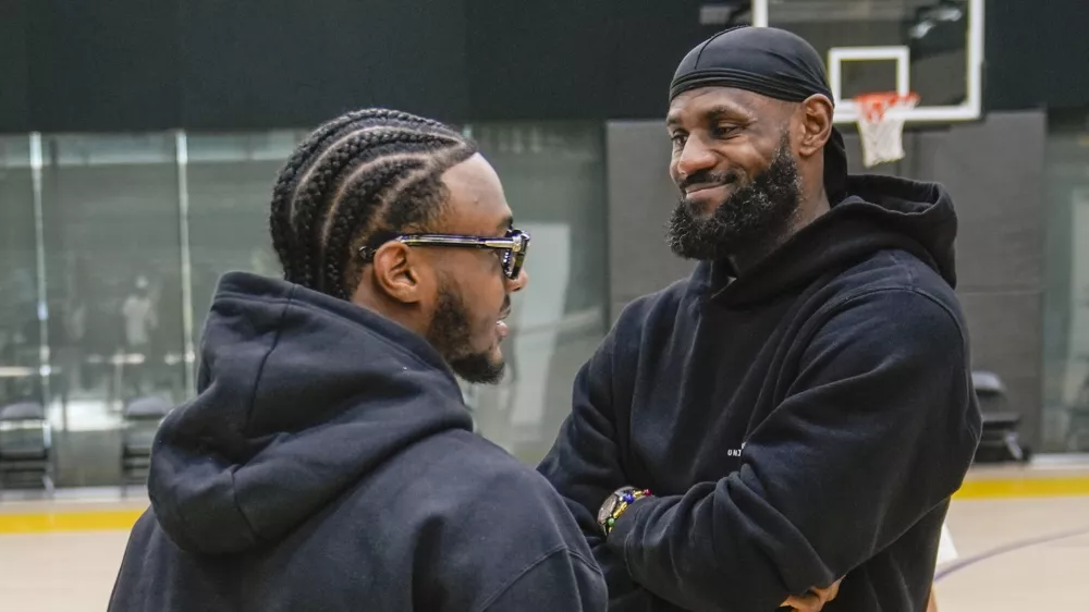 Los Angeles Lakers draft pick Bronny James, left, and his father, LeBron James, share a light moment as they arrive for the NBA basketball team's news conference in El Segundo, Calif., Tuesday, July 2, 2024 (AP Photo/Damian Dovarganes)