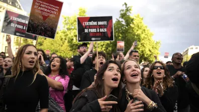 People react to the projection of results during the second round of the legislative elections, near Republique Plaza in Paris, France. Polls have closed in France, and polling projections say a coalition on the left that came together unexpectedly has won the most parliamentary seats in the pivotal runoff elections after a high turnout among voters. Sign reads "The extreme right shall not pass. From Gaza to Paris Intifada". (AP Photo/Christophe Ena)