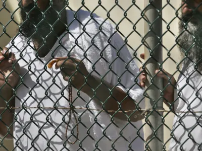 FILE - In this photo, reviewed by a US Department of Defense official, detainees stand together at a fence, one holding Islamic prayer beads, at Camp Delta prison, at the Guantanamo Bay U.S. Naval Base, Cuba, on Tuesday, Sept. 19, 2006. A 74-year-old from Pakistan who was the oldest prisoner at the Guantanamo Bay detention center was released and returned to Pakistan on Saturday, the foreign ministry in Islamabad said Saturday, Oct. 29, 2022. (AP Photo/Brennan Linsley, File)