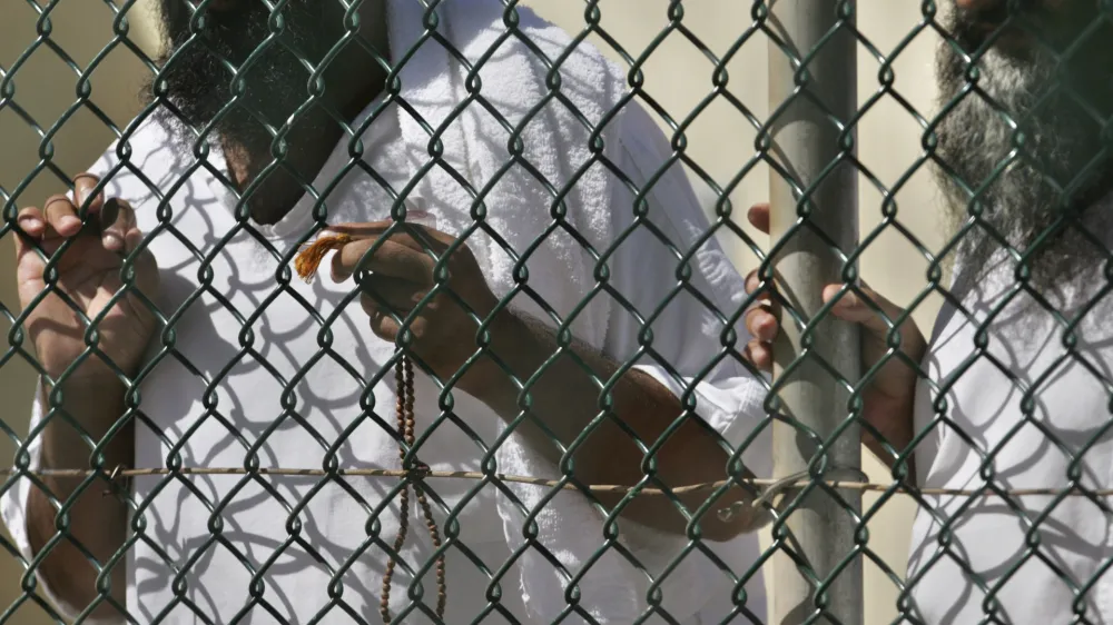 FILE - In this photo, reviewed by a US Department of Defense official, detainees stand together at a fence, one holding Islamic prayer beads, at Camp Delta prison, at the Guantanamo Bay U.S. Naval Base, Cuba, on Tuesday, Sept. 19, 2006. A 74-year-old from Pakistan who was the oldest prisoner at the Guantanamo Bay detention center was released and returned to Pakistan on Saturday, the foreign ministry in Islamabad said Saturday, Oct. 29, 2022. (AP Photo/Brennan Linsley, File)