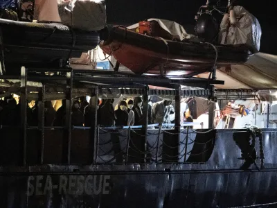 Migrants stand on the deck of the Humanity 1 rescue ship run by the German organization SOS Humanitarian, at harbor in the port of Catania, Sicily, southern Italy, early Sunday, Oct. 6, 2022. Italy allowed the Humanity 1 rescue ship carrying over 100 migrants to enter the Sicilian port and begin disembarking minors, while refusing to respond to requests for safe harbor from three other ships carrying 900 more people in nearby waters. (AP Photo/Salvatore Cavalli)