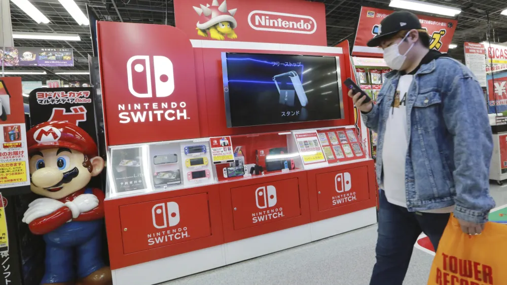 A man walks an advertisement of Nintendo Switch at an electronics retail chain store in Tokyo on Oct. 13, 2021. Japanese video game maker Nintendo recorded a 34% surge in fiscal first half profits Tuesday, Nov. 8, 2022, as products for its Switch console like "Splatoon 3," a paint-shooting game, sold well. (AP Photo/Koji Sasahara)