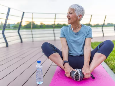 Relaxed athletic mature woman sitting on fitness mat outdoors. Senior Woman Resting After Exercises. Woman on a yoga mat to relax outdoor. Senior lady prefers healthy lifestyle