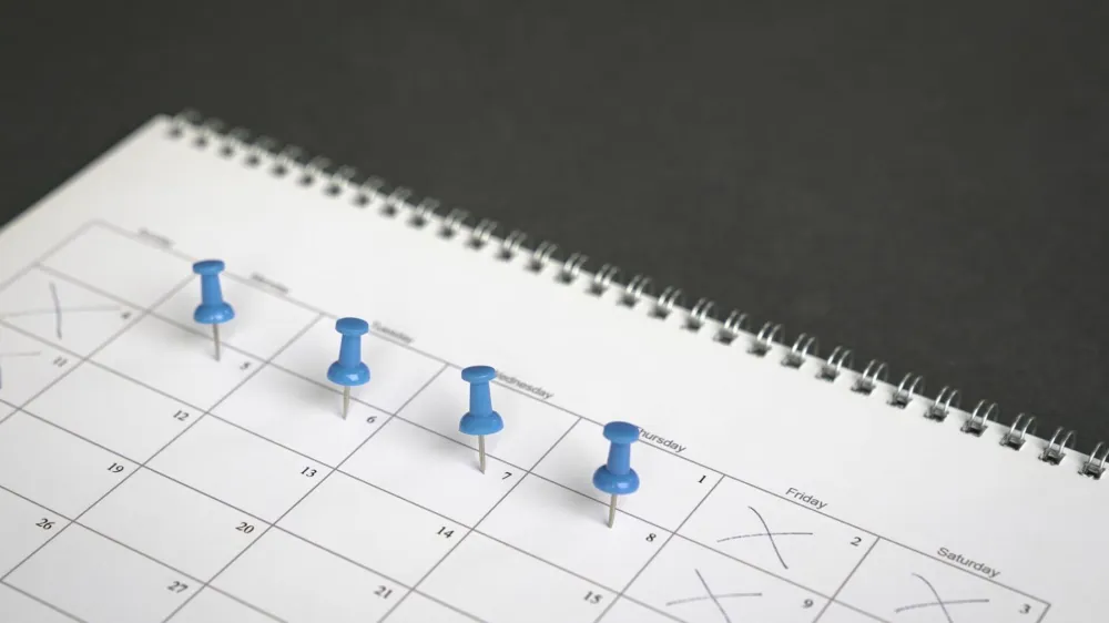 Blue pins on four days in a week on a calendar. Friday, Saturday and Sunday crossed out. Four day work week concept.