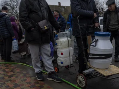 Residents queue to fill containers with drinking water in Kherson, southern Ukraine, Sunday, Nov. 20, 2022. Russian forces fired tank shells, rockets and other artillery on the city of Kherson, which was recently liberated from Ukrainian forces. (AP Photo/Bernat Armangue)