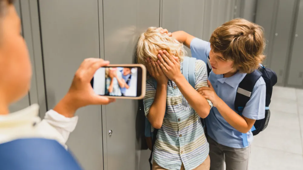 Schoolchildren cruel boys filming on the phone torturing bullying their classmate in school hall. Puberty difficult age