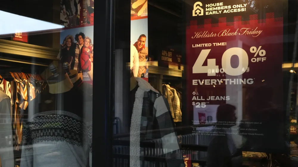 The reflections of passing shoppers are seen in the glass of a Hollister clothing store advertising sales, ahead of Black Friday and the Thanksgiving holiday, Monday, Nov. 21, 2022, in Miami. Retailers are ushering in the start of the holiday shopping season on the day after Thanksgiving, preparing for the biggest crowds since 2019. (AP Photo/Rebecca Blackwell)