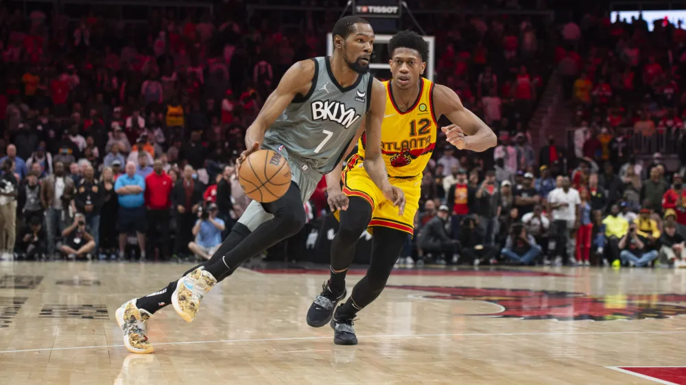 Brooklyn Nets forward Kevin Durant (7) dribbles past Atlanta Hawks forward De'Andre Hunter (12) during the second half of an NBA basketball game Saturday, April 2, 2022, in Atlanta. (AP Photo/Hakim Wright Sr.)