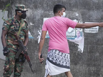 A Sri Lankan man interacts with an army soldier standing guard in a street during a curfew in Colombo, Sri Lanka, Sunday, April 3, 2022. Opposition lawmakers were marching Sunday protesting against the president's move to impose a curfew and state of emergency amid a worsening economic crisis. (AP Photo/Eranga Jayawardena)