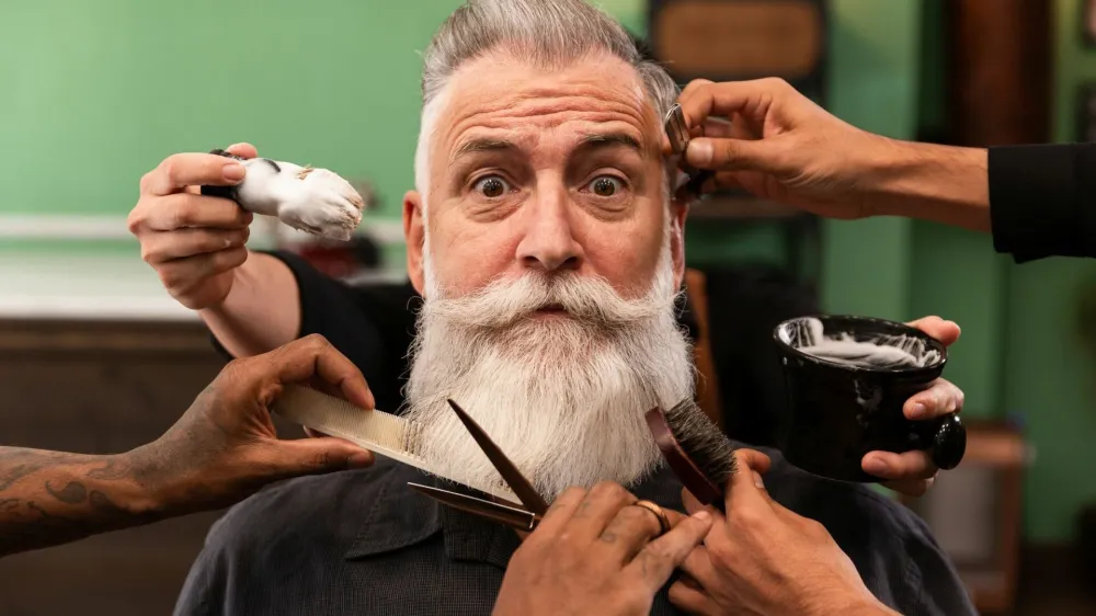 mature man with white beard looking at camera in barber shop with barber hands with cutting and shaving instruments, brush, scissors, comb, razor. hipster style