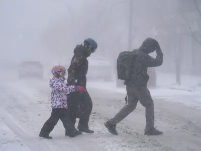 The Firestone family makes their way across Elmwood Avenue in Buffalo, N.Y. after stocking up on supplies at the grocery store, Friday, Dec. 23, 2022. Winter weather is blanketing the U.S. as a massive storm sent temperatures crashing and created whiteout conditions.(Derek Gee /The Buffalo News via AP)