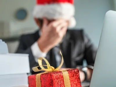 Sad and unhappy businessman with Santa Claus hat crying in office during Christmas holiday season, wrapped present on the desk with selective focus