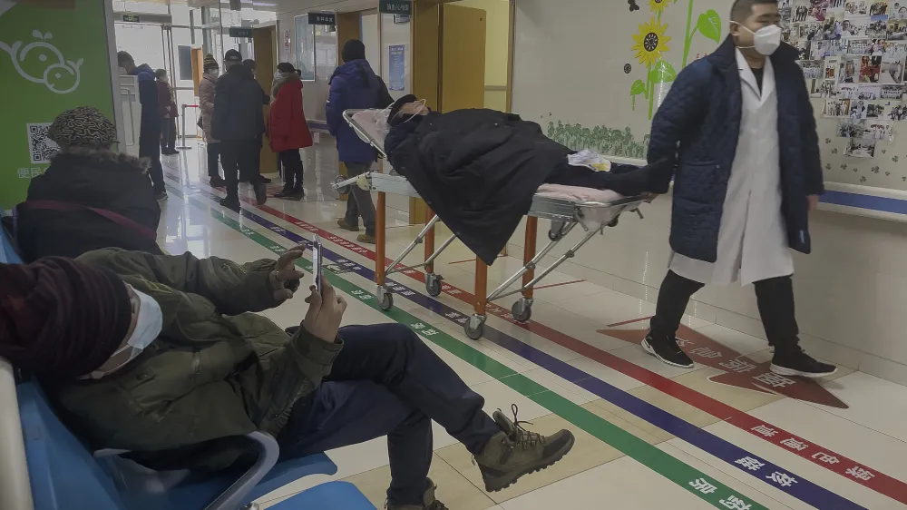 A man browses his smartphone as an elderly patient is wheeled to an emergency hall in a hospital in Beijing, Saturday, Jan. 7, 2023. China has suspended or closed the social media accounts of more than 1,000 critics of the government's policies on the COVID-19 outbreak, as the country moves to further open up. (AP Photo/Andy Wong)