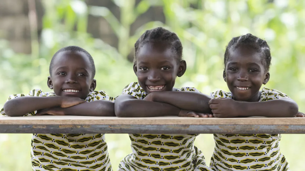 ﻿Three African children proudly sitting in their desk at school in Bamako, Mali. Candid outdoor shot of one boy and two girls learning their lessons at school.