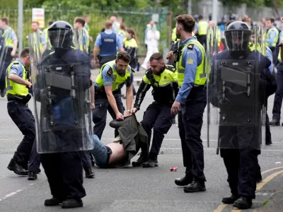 15 July 2024, Ireland, Dublin: Irish Gardai officers detain a protesters after a number of fires have been started at the former site of the Crown Paints factory in Coolock. Photo: Niall Carson/PA Wire/dpa