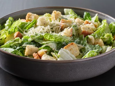 fresh caesar salad with croutons and parmesan cheese in bowl on dark table top / Foto: Rez-art