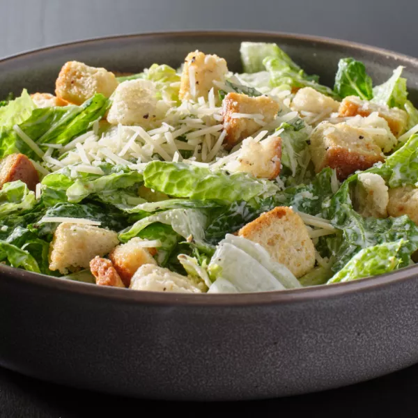 fresh caesar salad with croutons and parmesan cheese in bowl on dark table top / Foto: Rez-art