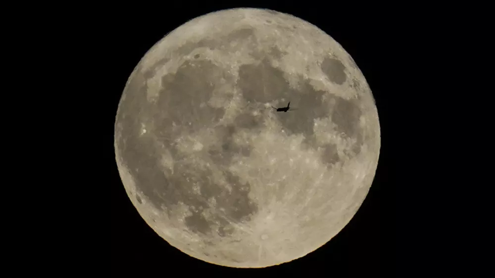 FILE - A plane passes in front of the moon, Aug. 30, 2023, in Chicago. Scientists have confirmed a cave on the moon, not far from where Neil Armstrong and Buzz Aldrin landed 55 years ago this week, and suspect there are hundreds more that could house future astronauts. (AP Photo/Kiichiro Sato, file)