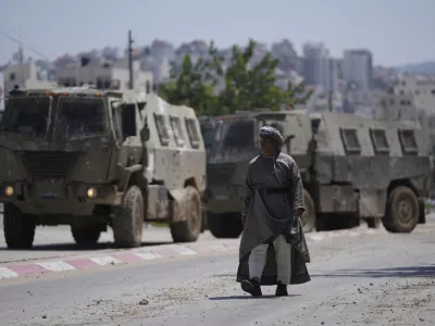 A Palestinian man walks past two army personal carriers during an Israeli army raid in the occupied West Bank refugee camp of Tulkarem, in Tulkarem, Tuesday, July 23, 2024. (AP Photo/Nasser Nasser)