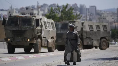 A Palestinian man walks past two army personal carriers during an Israeli army raid in the occupied West Bank refugee camp of Tulkarem, in Tulkarem, Tuesday, July 23, 2024. (AP Photo/Nasser Nasser)