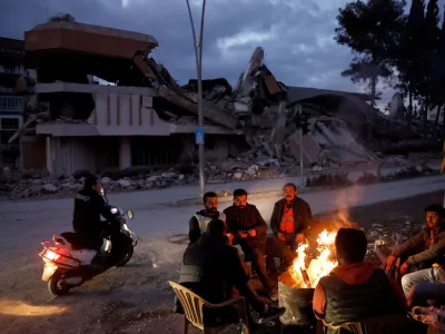 People warm themselves by a fire beside a collapsed building and rubble, in the aftermath of a deadly earthquake, in Antakya, Hatay province, Turkey, February 21, 2023. REUTERS/Clodagh Kilcoyne