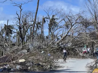 In this handout photo provided by the Office of the Vice President, a man walks past toppled trees due to Typhoon Rai in Siargao island, Surigao del Norte, southern Philippines on Sunday Dec. 19, 2021. A strong typhoon engulfed villages in floods that trapped residents on roofs, toppled trees and knocked out power in southern and central island provinces, where more than 300,000 villagers had fled to safety before the onslaught, officials said. (Office of the Vice President via AP)