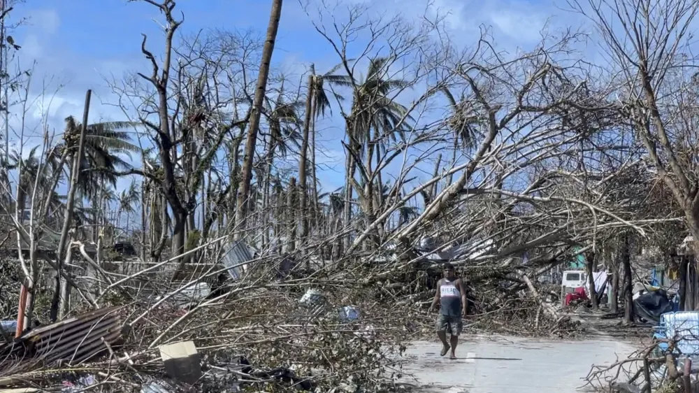 In this handout photo provided by the Office of the Vice President, a man walks past toppled trees due to Typhoon Rai in Siargao island, Surigao del Norte, southern Philippines on Sunday Dec. 19, 2021. A strong typhoon engulfed villages in floods that trapped residents on roofs, toppled trees and knocked out power in southern and central island provinces, where more than 300,000 villagers had fled to safety before the onslaught, officials said. (Office of the Vice President via AP)