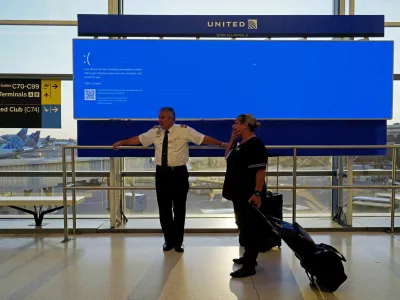 United Airlines employees wait by a departures monitor displaying a blue error screen, also known as the "Blue Screen of Death" inside Terminal C in Newark International Airport, after United Airlines and other airlines grounded flights due to a worldwide tech outage caused by an update to CrowdStrike's "Falcon Sensor" software which crashed Microsoft Windows systems, in Newark, New Jersey, U.S., July 19, 2024. REUTERS/Bing Guan   TPX IMAGES OF THE DAY