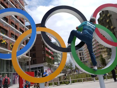 Regis Scott, a polyclinic medical team member, climbs the Olympic rings for a photo, in the Olympic Village at the 2024 Summer Olympics, Tuesday, July 23, 2024, in Paris, France. (AP Photo/Rebecca Blackwell)