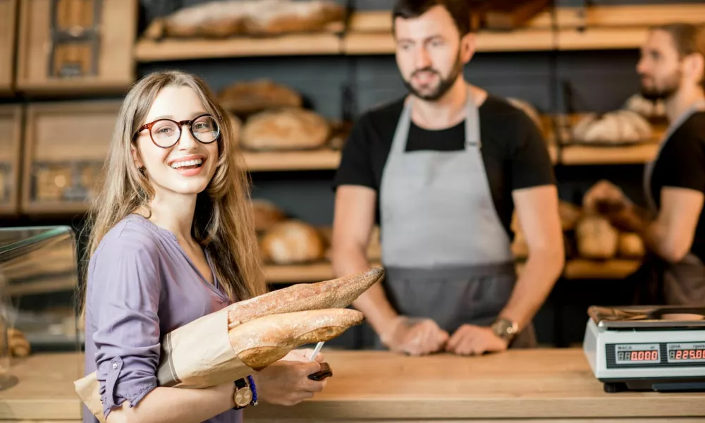 Portrait of a happy woman client buying bread at the bakery shop with handsome male sellers / Foto: Rosshelen