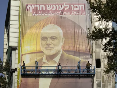 Iranian workers install a huge banner on a wall showing a portrait of Hamas leader Ismail Haniyeh and the Dome of Rock Mosque at the Al-Aqsa Mosque compound of Jerusalem with a sign which reads in Farsi and Hebrew: "Wait for severe punishment," at Felestin (Palestine) Sq. in Tehran, Iran, Wednesday, July 31, 2024. Haniyeh was assassinated in Tehran, Iran's paramilitary Revolutionary Guard said early Wednesday. (AP Photo/Vahid Salemi)