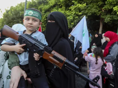 A supporter of the Islamist Hamas movement carries her son, who holds a machine gun toy during a protest in the southern port city of Sidon, Lebanon, Wednesday, July 31, 2024, to condemn the killing of Hamas political chief Ismail Haniyeh. Two back-to-back strikes in Beirut and Tehran, both attributed to Israel and targeting high-ranking figures in Hezbollah and Hamas, have left Hezbollah and Iran in a quandary. (AP Photo/Mohammed Zaatari)