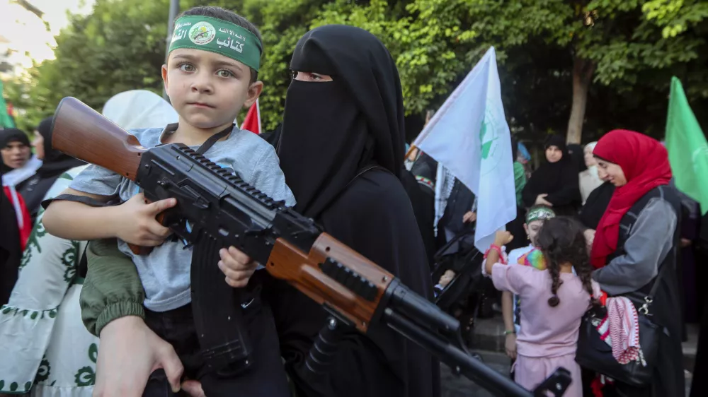 A supporter of the Islamist Hamas movement carries her son, who holds a machine gun toy during a protest in the southern port city of Sidon, Lebanon, Wednesday, July 31, 2024, to condemn the killing of Hamas political chief Ismail Haniyeh. Two back-to-back strikes in Beirut and Tehran, both attributed to Israel and targeting high-ranking figures in Hezbollah and Hamas, have left Hezbollah and Iran in a quandary. (AP Photo/Mohammed Zaatari)