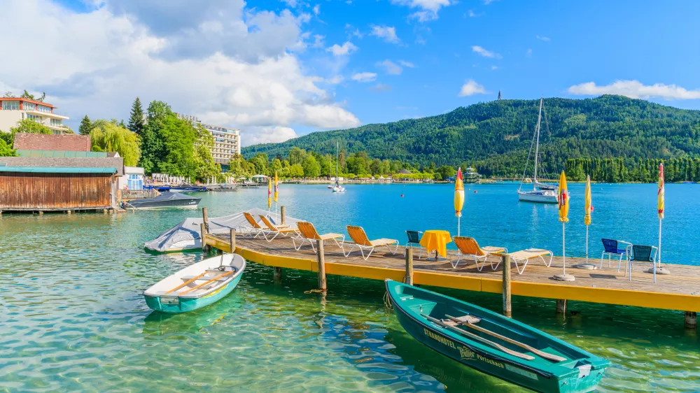 WORTHERSEE LAKE, AUSTRIA - JUN 20, 2015: tourist boats and sunchairs with umbrellas on wooden pier of beautiful alpine lake Wort