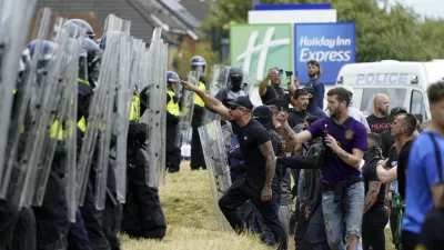 Demonstrators face police officers as trouble flares during an anti-immigration protest outside the Holiday Inn Express in Rotherham, England, Sunday Aug. 4, 2024. (Danny Lawson/PA via AP)