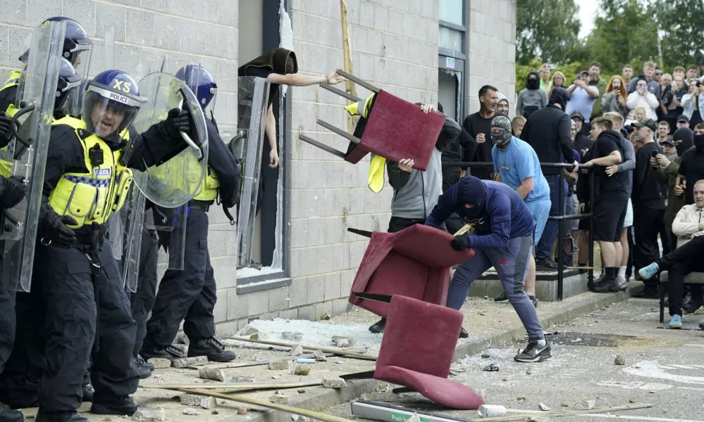 A chair is thrown at police officers as trouble flares during an anti-immigration protest outside the Holiday Inn Express in Rotherham, England, Sunday Aug. 4, 2024. (Danny Lawson/PA via AP)