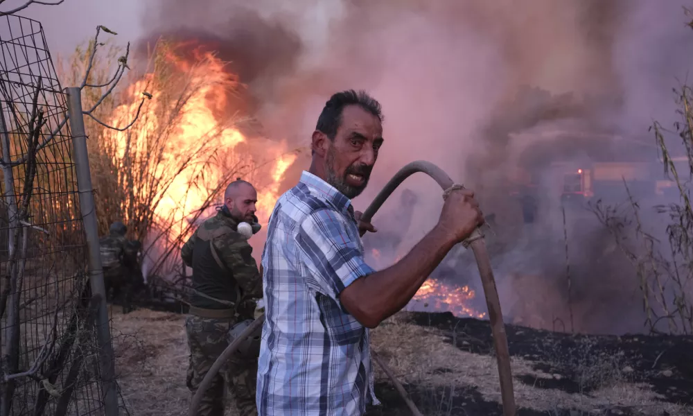 Volunteers try to extinguish the fire in northern Athens, Monday, Aug. 12, 2024, as hundreds of firefighters tackle a major wildfire raging out of control on fringes of Greek capital. (AP Photo/Aggelos Barai)