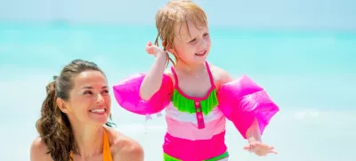 Baby girl shaking out water from ear on beach near mother / Foto: Centralitalliance