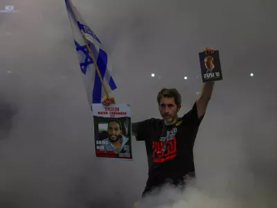 A man holds an Israeli national flag, and pictures of a hostage and Israeli Prime Minister Benjamin Netanyahu, as people demonstrate against Netanyahu's government and call for the release of hostages in Gaza, amid the Israel-Hamas conflict, in Tel Aviv, Israel, August 17, 2024. Picture taken with long exposure. REUTERS/Florion Goga