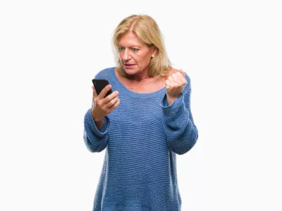 Middle age blonde woman sending message using smartphone over isolated background annoyed and frustrated shouting with anger, crazy and yelling with raised hand, anger concept / Foto: Aaronamat