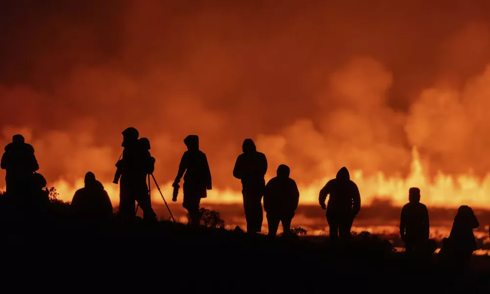 Tourists and visitors try to get a view of the eruption from a distance from the intersection between Reykjanesbraut, Iceland, and the road to Grindavik, Thursday, Aug. 22, 2024. (AP Photo/Marco di Marco)