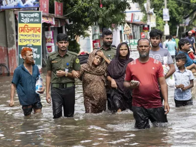 People carry their belongings and wade through flooded water to reach a temporary shelter in Feni, a coastal district in southeast Bangladesh, Friday, Aug. 23, 2024. (AP Photo/Fatima Tuj Johora)