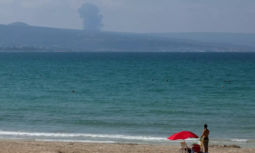 A view shows smoke on the Lebanese side of the border with Israel, as a man stands at a beach in Tyre, amid ongoing cross-border hostilities between Hezbollah and Israeli forces, southern Lebanon August 25, 2024. REUTERS/Aziz Taher