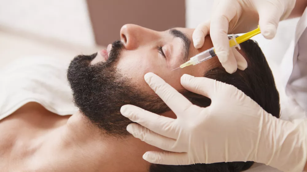 Bearded man getting anti-wrinkle face filler treatment by beautician / Foto: Oleksandra Polishchuk