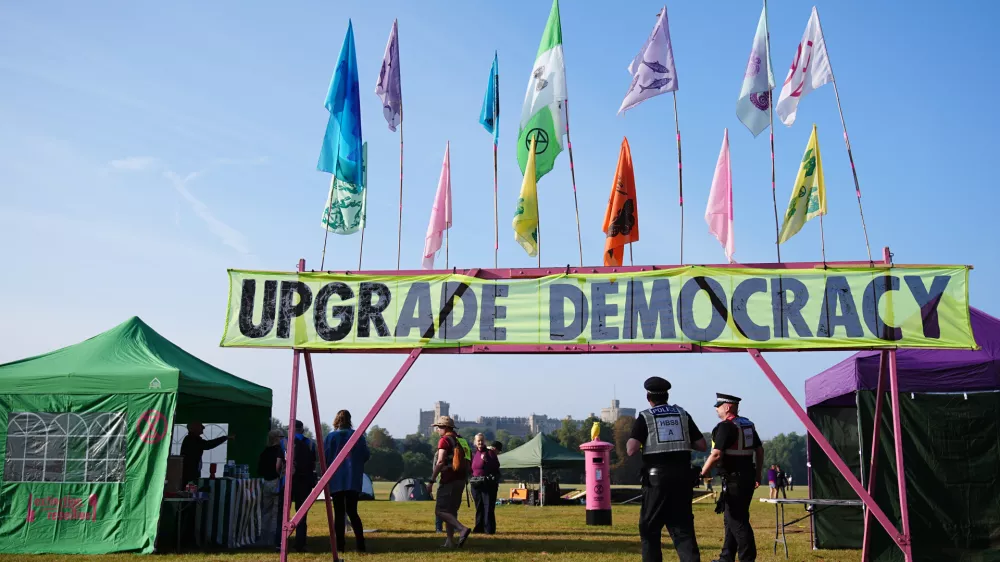 30 August 2024, United Kingdom, Windsor: Police officers walk beneath a banner reading 'upgrade democracy', among tents in Windsor Great Park, as Extinction Rebellion stage a mass occupation. Activists are calling for the Government to create and be led by a citizens' assembly on climate and ecological justice. Photo: Aaron Chown/PA Wire/dpa